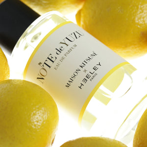 Heeley - Maison Kitsuné - Note de Yuzu Parfumflakon umgeben von frischen Yuzu-Zitronen in hellem Licht