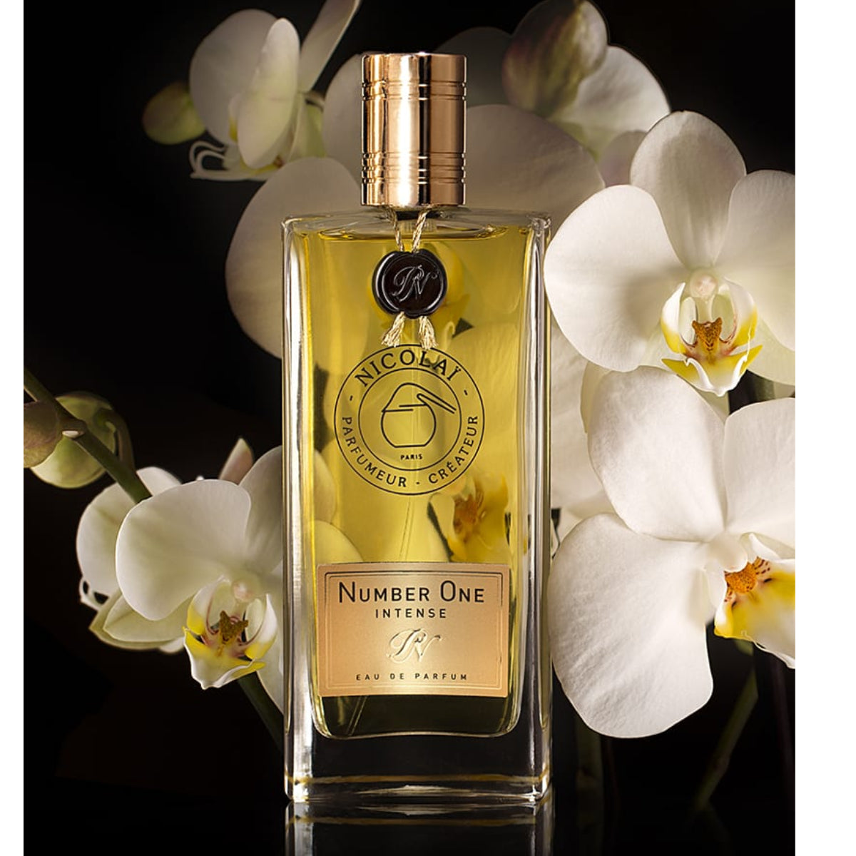 Nicolaï Number One Intense Eau de Parfum in tall rectangular bottle with gold cap and black seal by white orchids on dark background