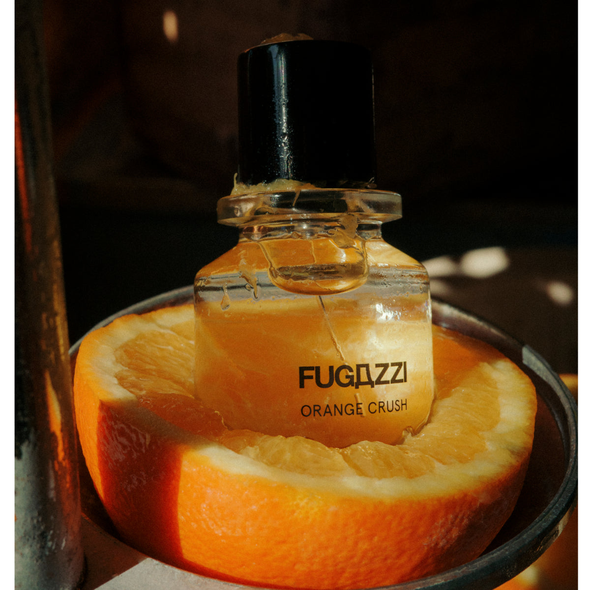 Fugazzi - Orange Crush Extrait Parfumflakon im Glas mit schwarzem Verschluss auf orangefarbener Frucht im Schattenlicht