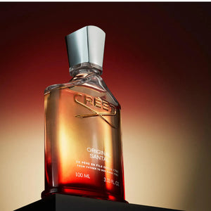 Creed - Original Santal Parfumflakon mit warmem Farbverlauf und silberfarbenem Verschluss vor dunklem Hintergrund