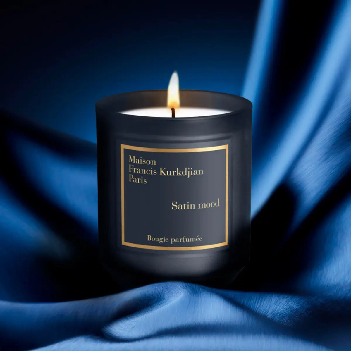 Maison Francis Kurkdjian Paris - Oud Satin Mood - Duftkerze im dunklen Glas mit sanft brennender Flamme auf blauem Satinstoff