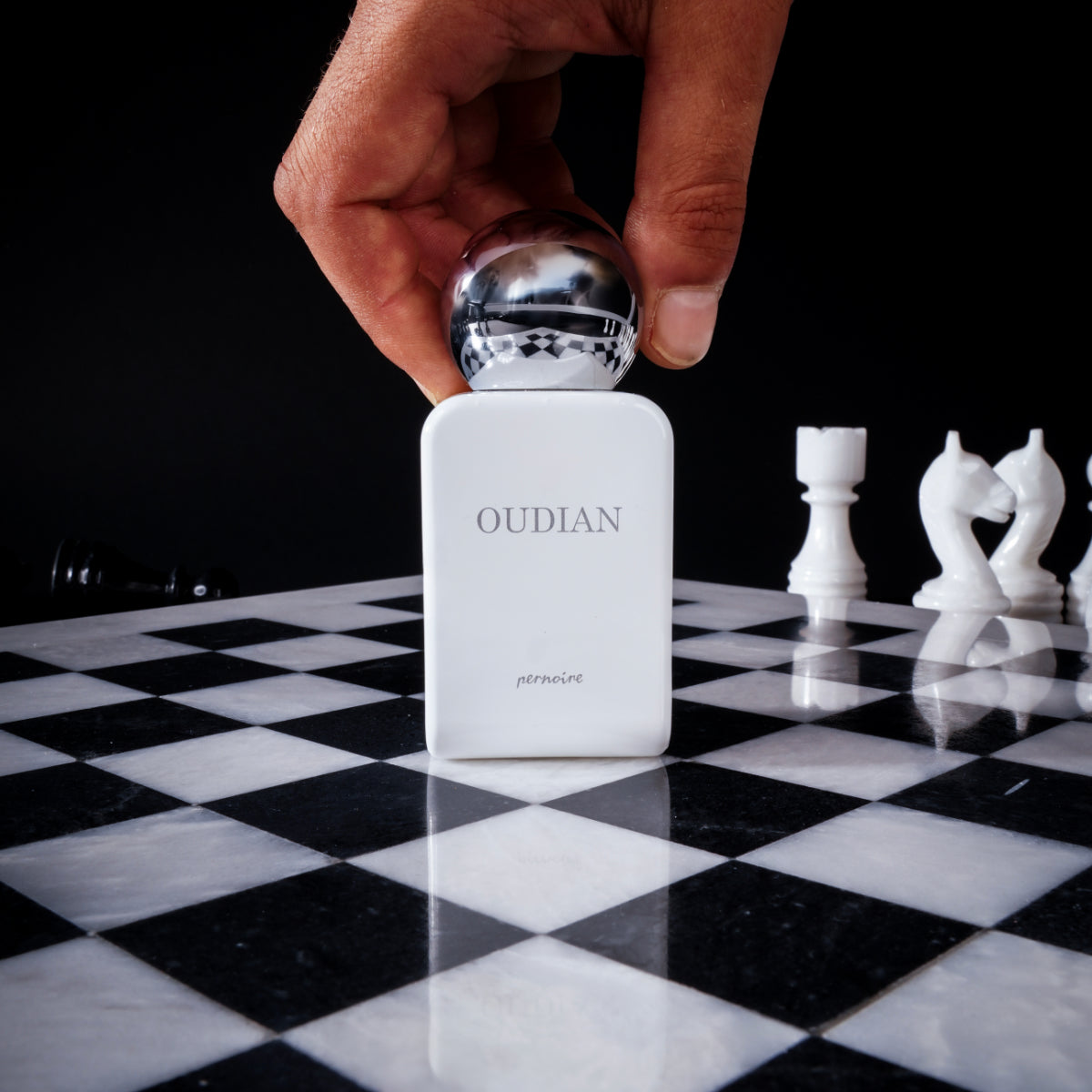 Pernoire - Odus Collection - Oudian Parfumflakon mit glänzendem rundem Verschluss auf Schachbrettmuster vor schwarzem Hintergrund