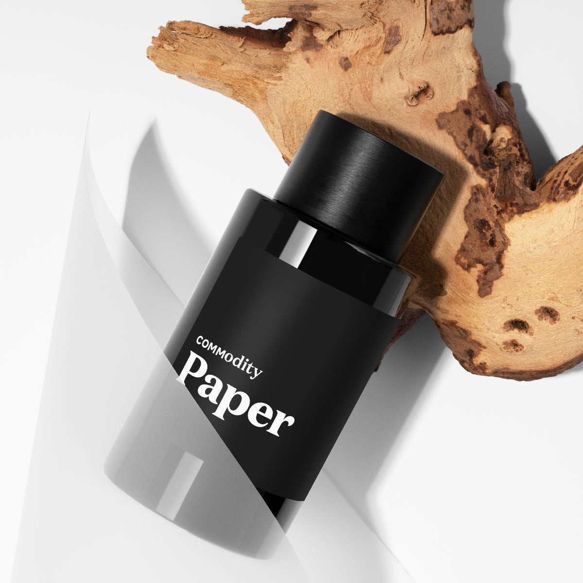 Commodity - Paper Parfumflakon in schlichtem schwarzen Design mit natürlichem Holzdetail auf hellgrauem Untergrund präsentiert