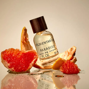 Pigmentarium - Paradiso zeigt Parfümflakon mit hellem Duftöl und dunklem Holzverschluss neben aufgeschnittener Grapefruit