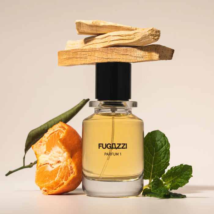 Fugazzi - Parfum 1 mit klarer Flasche, schwarzem Deckel, Mandarine, Holz und frischen grünen Blättern vor hellem Hintergrund