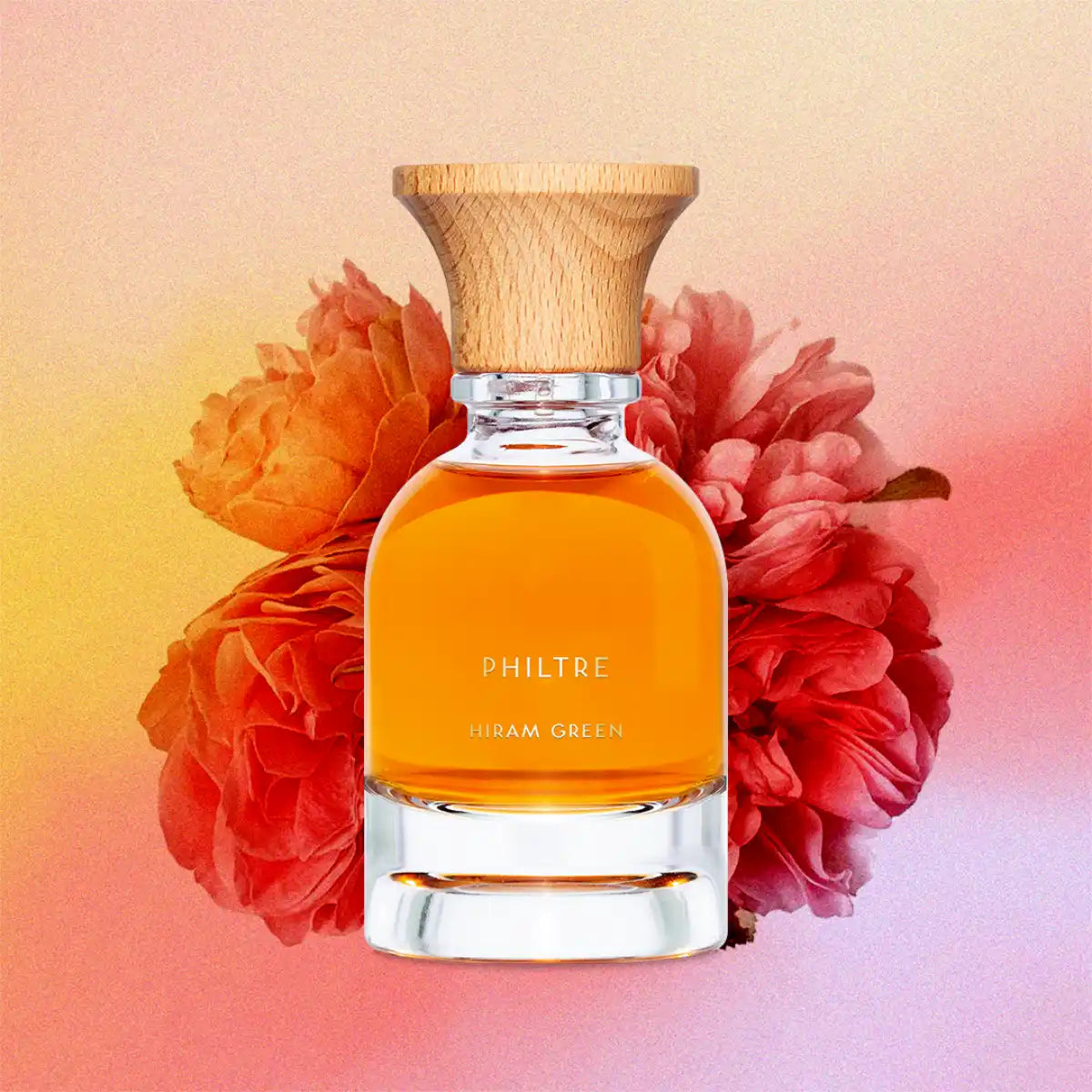 Hiram Green - Philtre Parfumflakon mit bernsteinfarbener Flüssigkeit und naturfarbenem Holzverschluss vor floralem Hintergrund