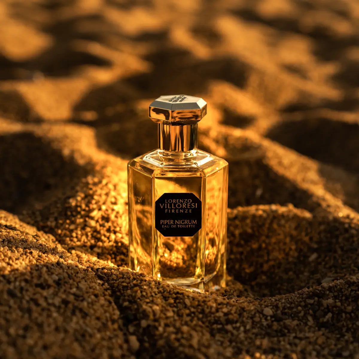 Lorenzo Villoresi Piper Nigrum Eau de Toilette in clear faceted bottle with gold hexagonal cap on textured sandy background