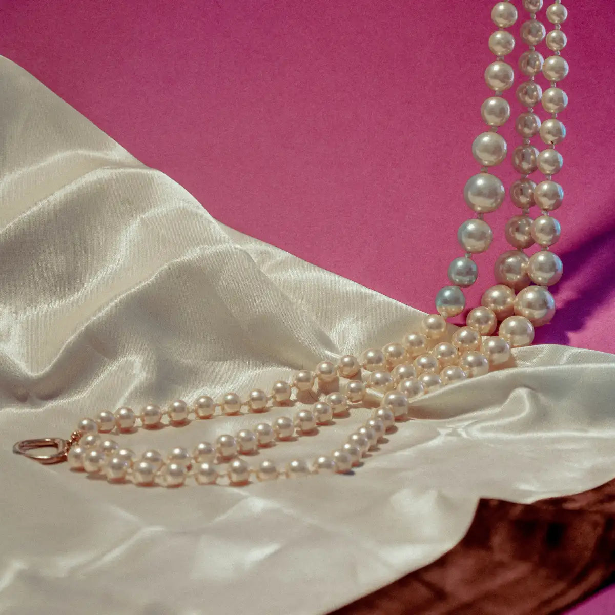 Sous Le Manteau - Poudre Impériale elegante Perlenkette auf seidigem Stoff vor pinkem Hintergrund
