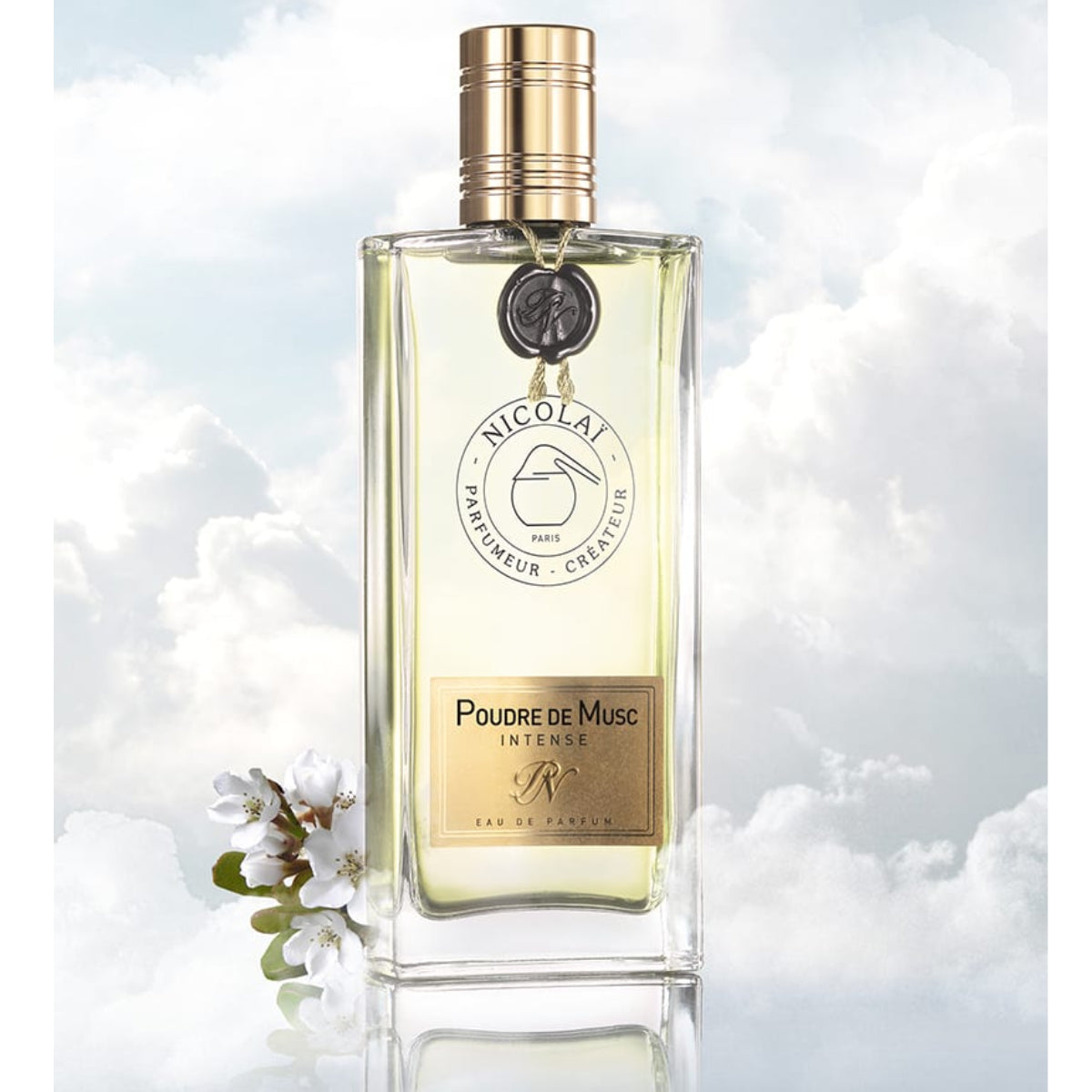 Nicolaï - Poudre de Musc Intense eleganter Flakon mit goldenem Verschluss vor wolkigem Himmel und weißen Blüten