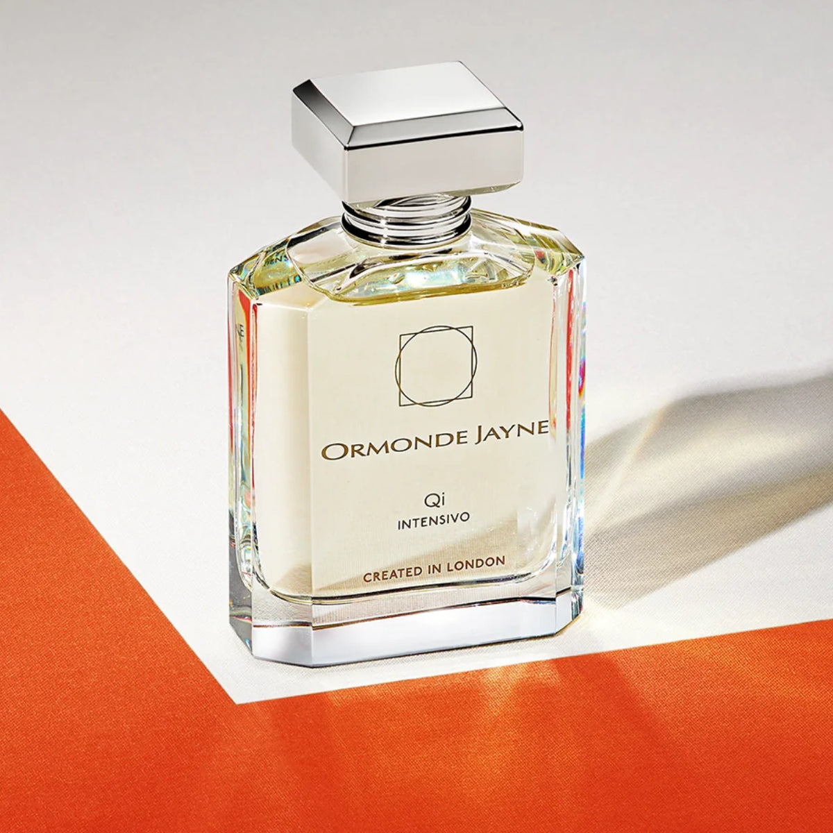 Ormonde Jayne - Qi Intensivo Parfumflakon mit klarem Glas und silberfarbenem Deckel auf weiß-orangefarbenem Untergrund