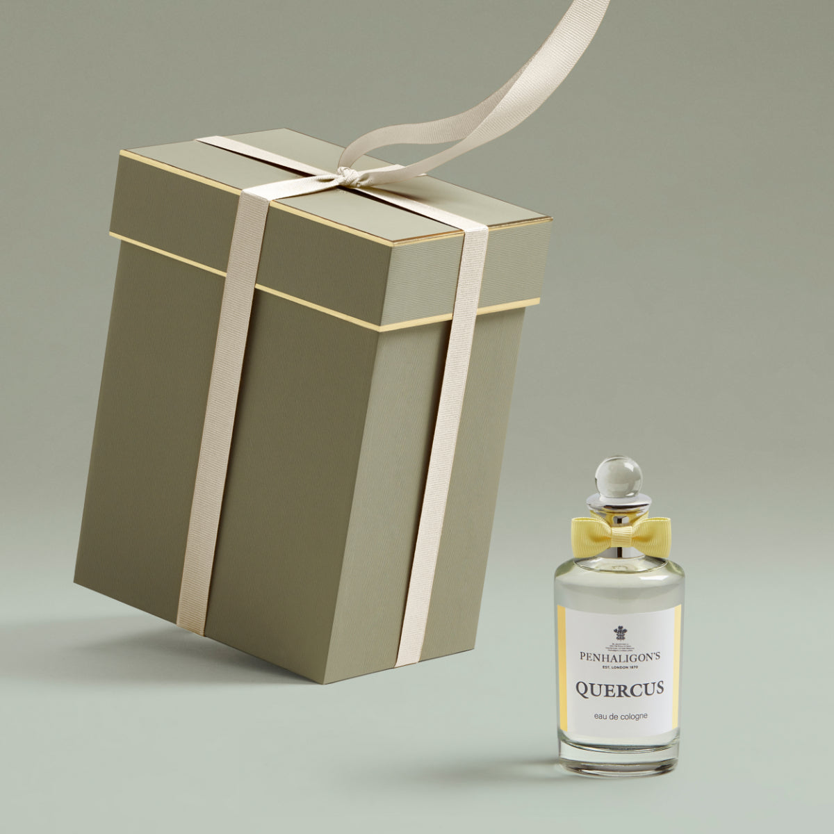 Penhaligon's Quercus eau de cologne in clear bottle with yellow bow beside pale green gift box with cream ribbon on gray background