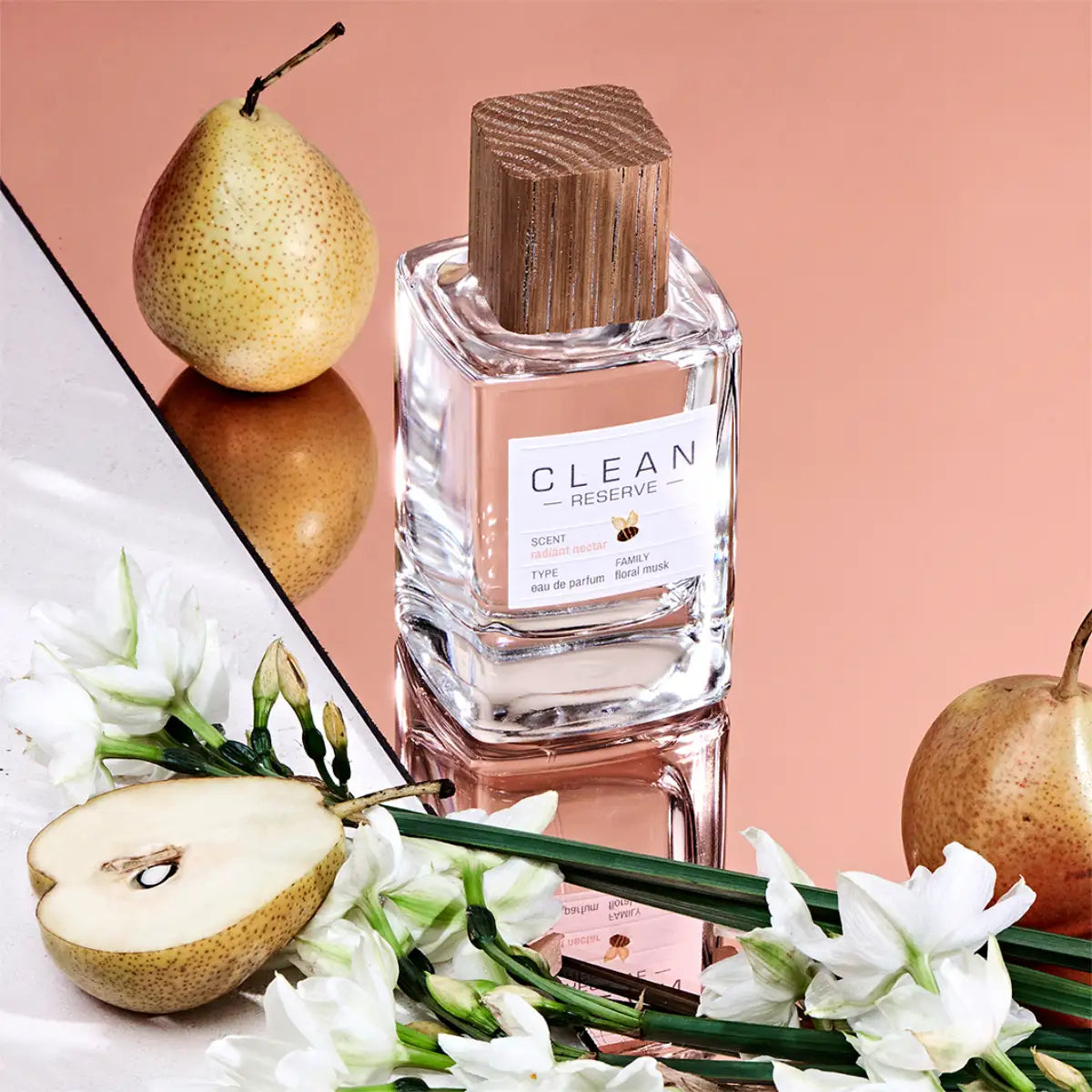 Clean Perfume - Reserve - Radiant Nectar Flakon mit Holzverschluss, umgeben von Birnen und weißen Blüten auf reflektierender Fläche