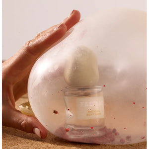 Fascent - Radical Softness Parfumflakon mit samtigem Deckel im transparenten Ballon mit roten Akzenten und zarter Hand davor