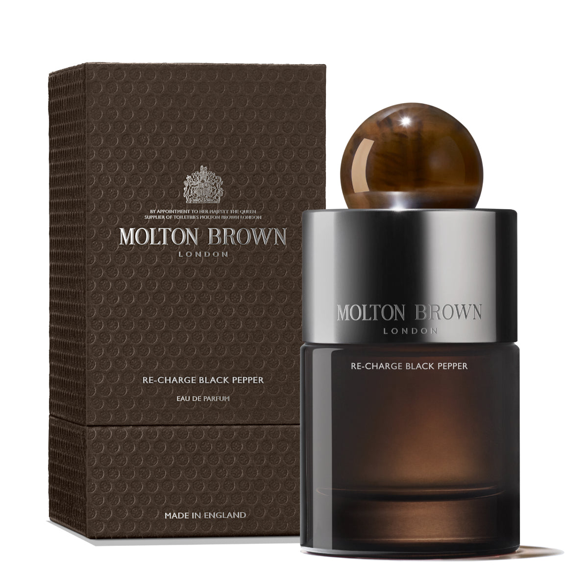 Molton Brown - Re-Charge Black Pepper Parfumflakon mit dunklem Glas und braunem kugelförmigem Verschluss neben strukturierter brauner Verpackung