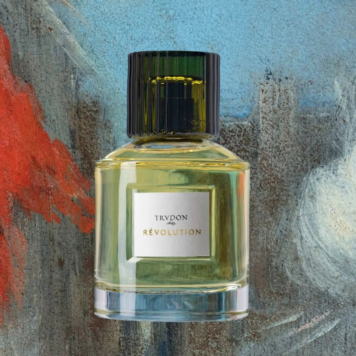Trudon - Révolution Parfumflakon mit grünem geriffeltem Verschluss vor farbenfrohem künstlerischem Hintergrund
