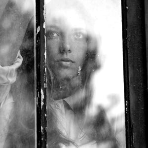 Carner Barcelona - Rima XI emotionale Schwarzweißaufnahme einer Frau hinter einem alten Fenster mit geheimnisvollem Ausdruck