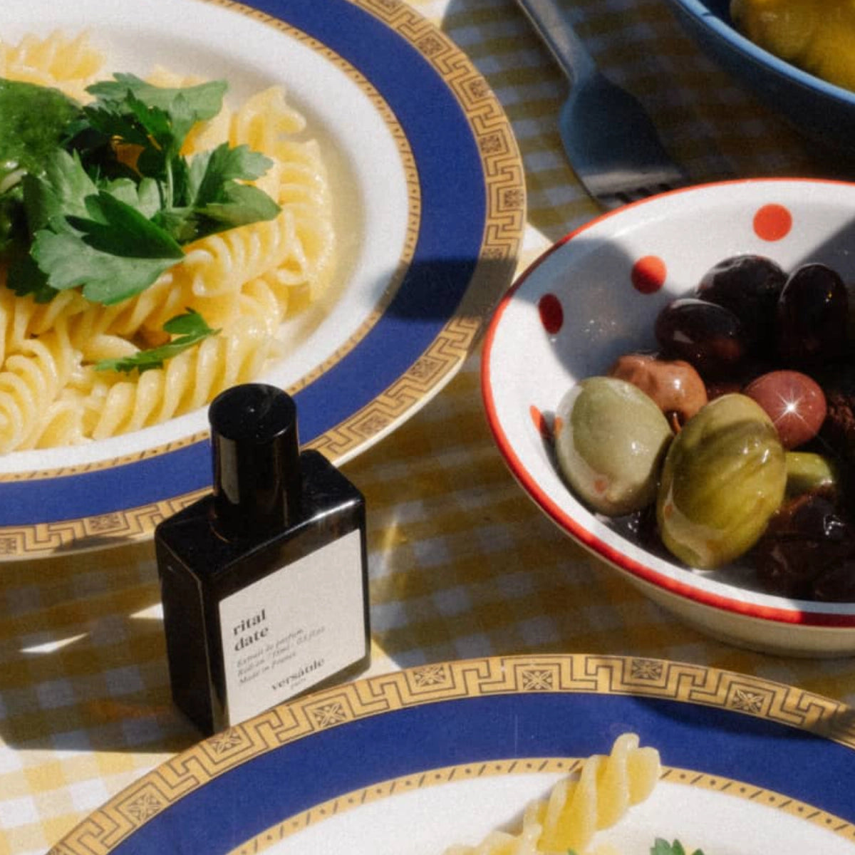 Versatile - Rital Date Flakon neben Teller mit Pasta und Schale mit Oliven auf kariertem Tischtuch