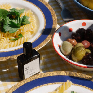 Versatile - Rital Date Flakon neben Teller mit Pasta und Schale mit Oliven auf kariertem Tischtuch