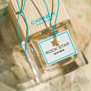 Carner Barcelona - Mediterranean Collection - Rock Star Parfumflakon mit Holzdeckel und kleinem Seesternanhänger vor Sandhintergrund