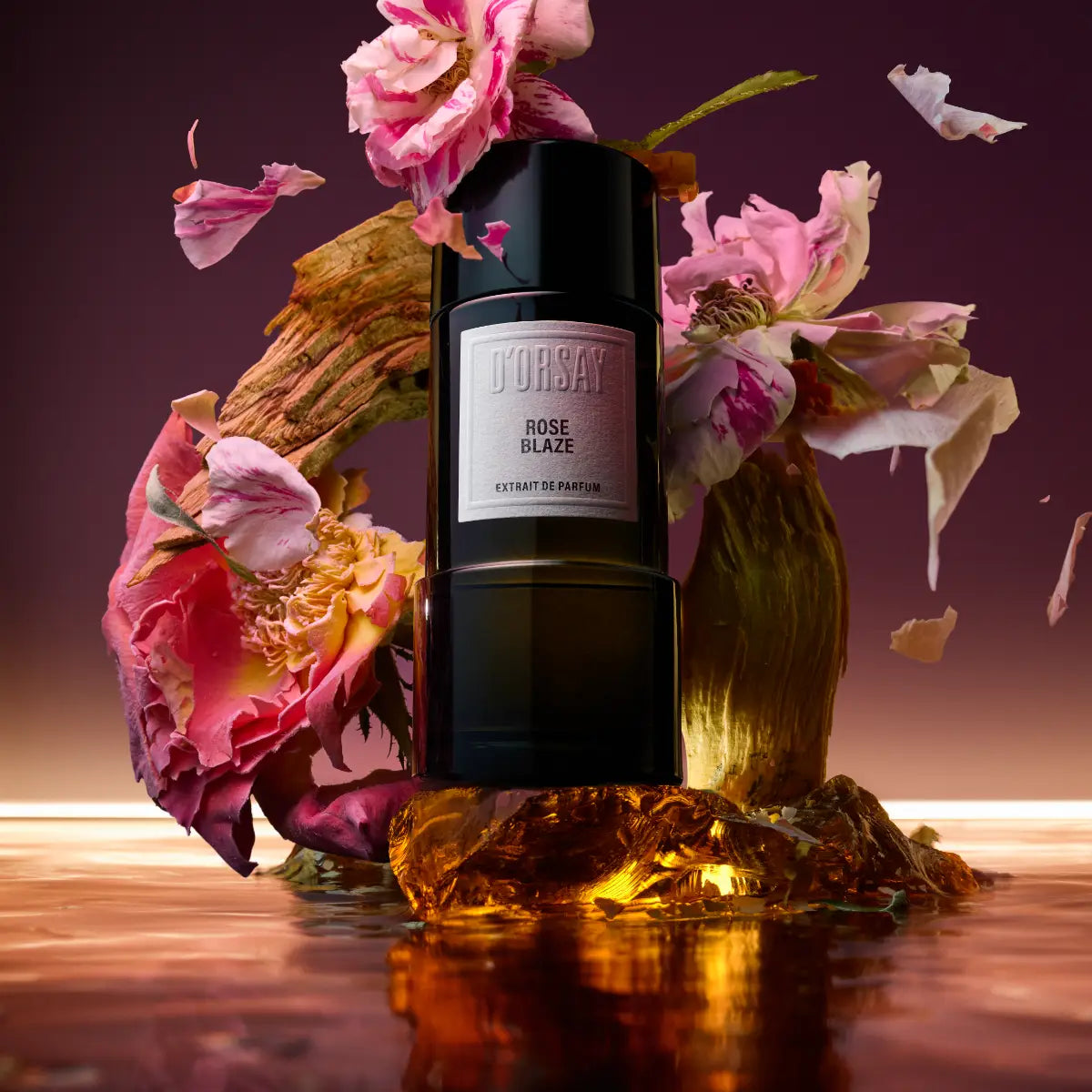 D'Orsay - Rose Blaze Extrait de Parfum in schwarzem Flakon umgeben von rosa Blüten und warmem Licht vor dunklem Hintergrund