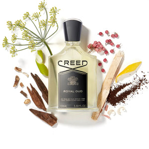 Creed - Royal Oud klarer Flakon mit schwarzem Etikett eingerahmt von Holz und Gewürzen auf weißem Hintergrund