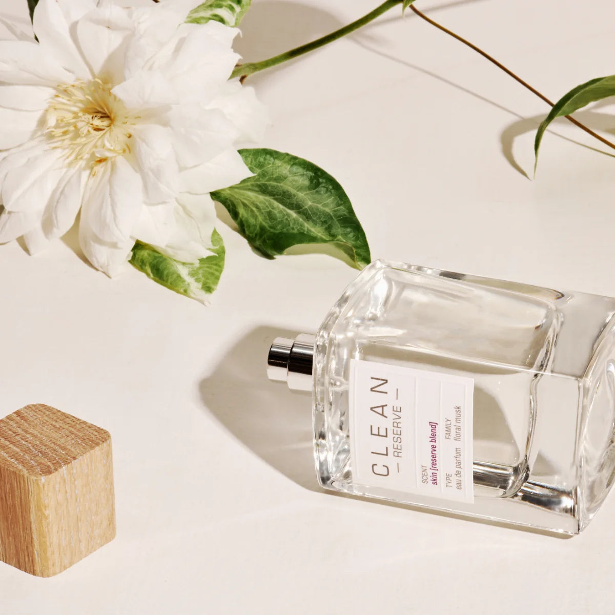 Clean Perfume - Reserve - skin [reserve blend] Parfumflakon neben weißer Blume und Holzblock auf hellem Untergrund