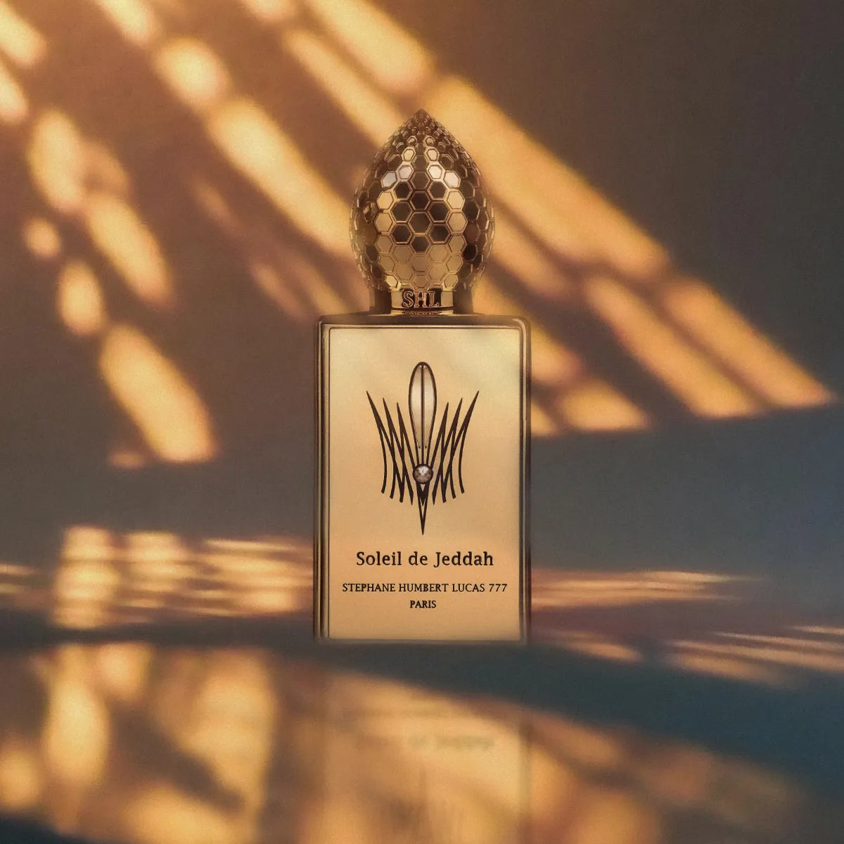 Stéphane Humbert Lucas 777 - Soleil de Jeddah zeigt eleganten Flakon mit goldfarbenem Wabenverschluss im warmen Lichtspiel