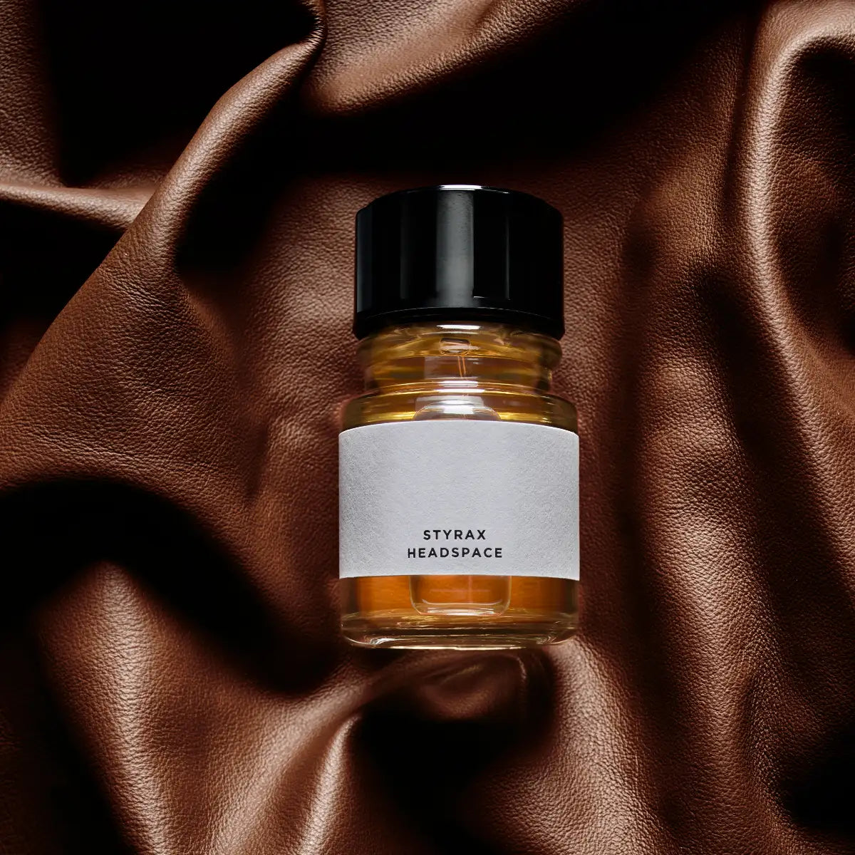 Headspace - Styrax Flakon mit bernsteinfarbener Flüssigkeit und schwarzem Verschluss auf braunem Lederhintergrund