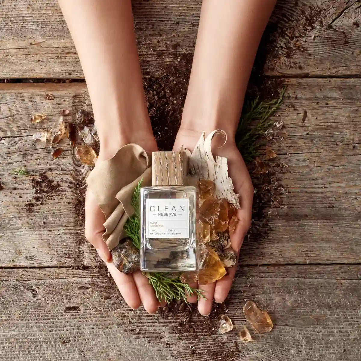 Clean Perfume - Reserve - Sueded Oud Parfumflakon mit Holzverschluss in Händen auf rustikalem Holz und Naturmaterialien