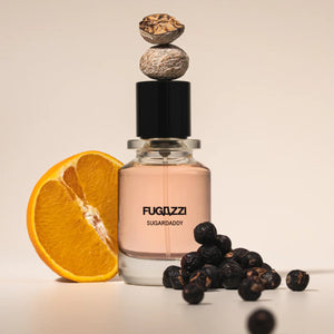 Fugazzi - Sugardaddy Parfumflakon mit sanft rosafarbenem Duft, umgeben von Orange und getrockneten Beeren vor hellem Hintergrund