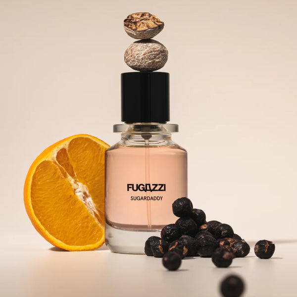 Fugazzi - Sugardaddy Parfumflakon mit sanft rosafarbenem Duft, umgeben von Orange und getrockneten Beeren vor hellem Hintergrund