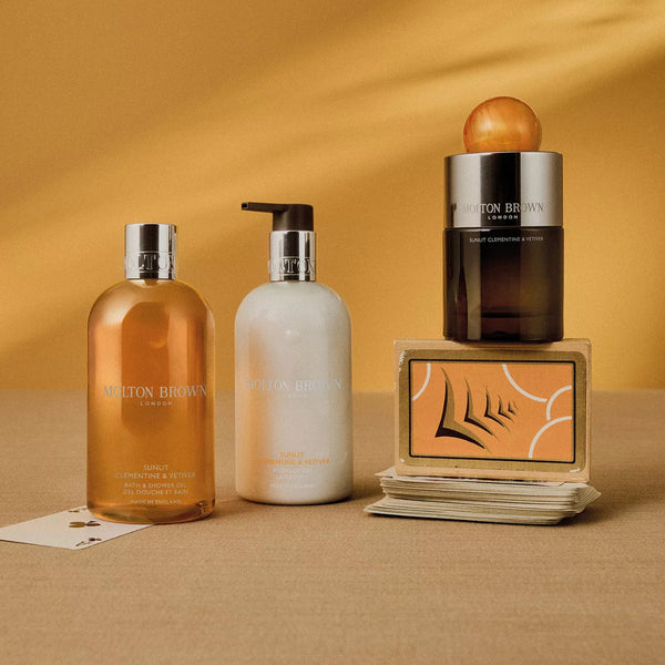 Molton Brown - Sunlit Clementine & Vetiver Body Lotion elegante Flasche mit dezentem Zitrusduft vor warmem Hintergrund