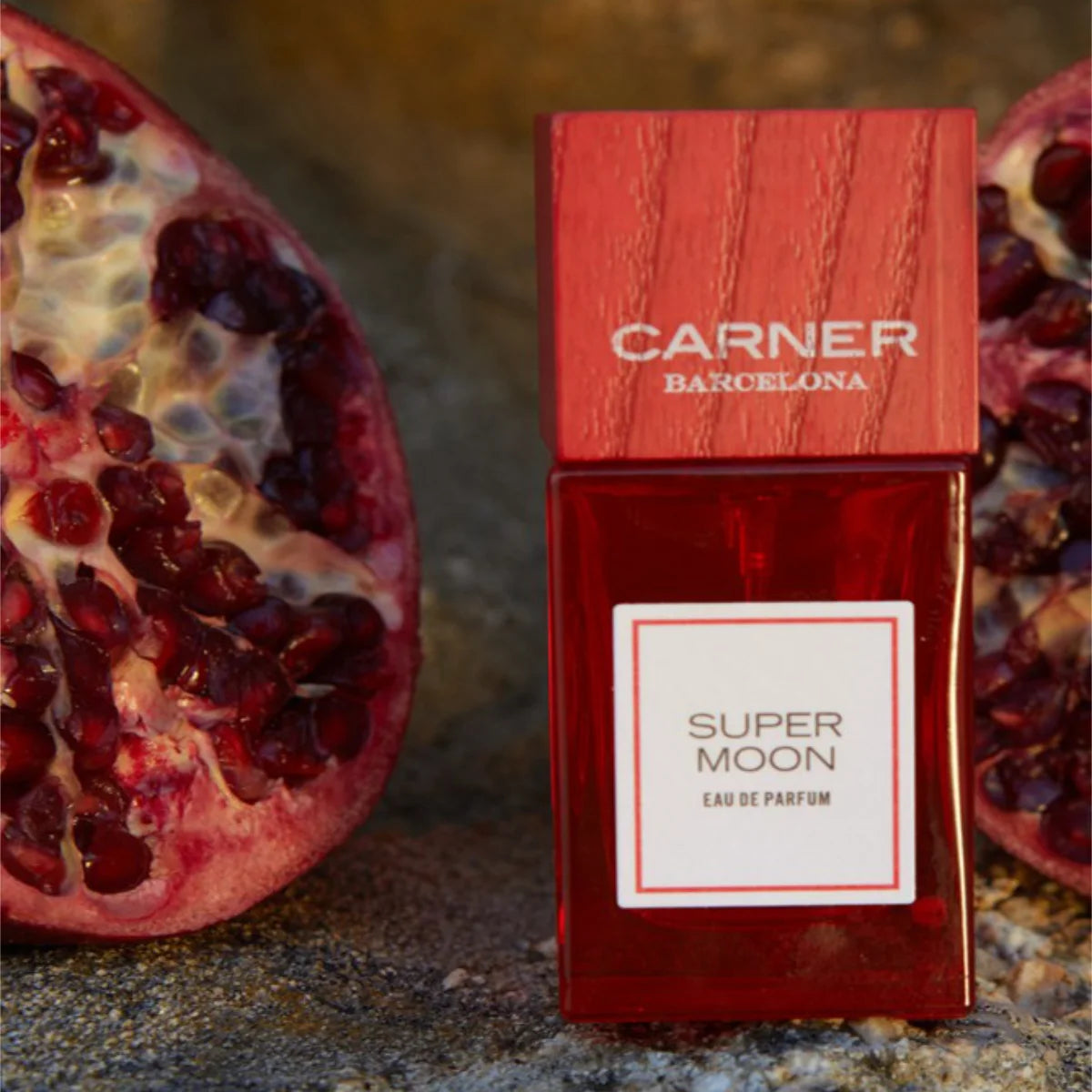 Carner Barcelona - Summer Journey Collection - Super Moon Parfum in rotem Flakon mit Holzdeckel neben aufgeschnittenem Granatapfel