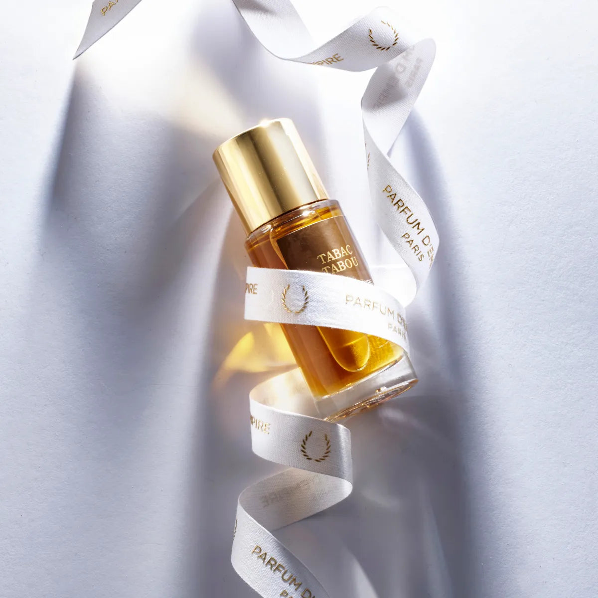 Parfum d'Empire - Tabac Tabou Flakon mit goldfarbenem Verschluss und bernsteinfarbenem Duftöl, umhüllt von weißem Band