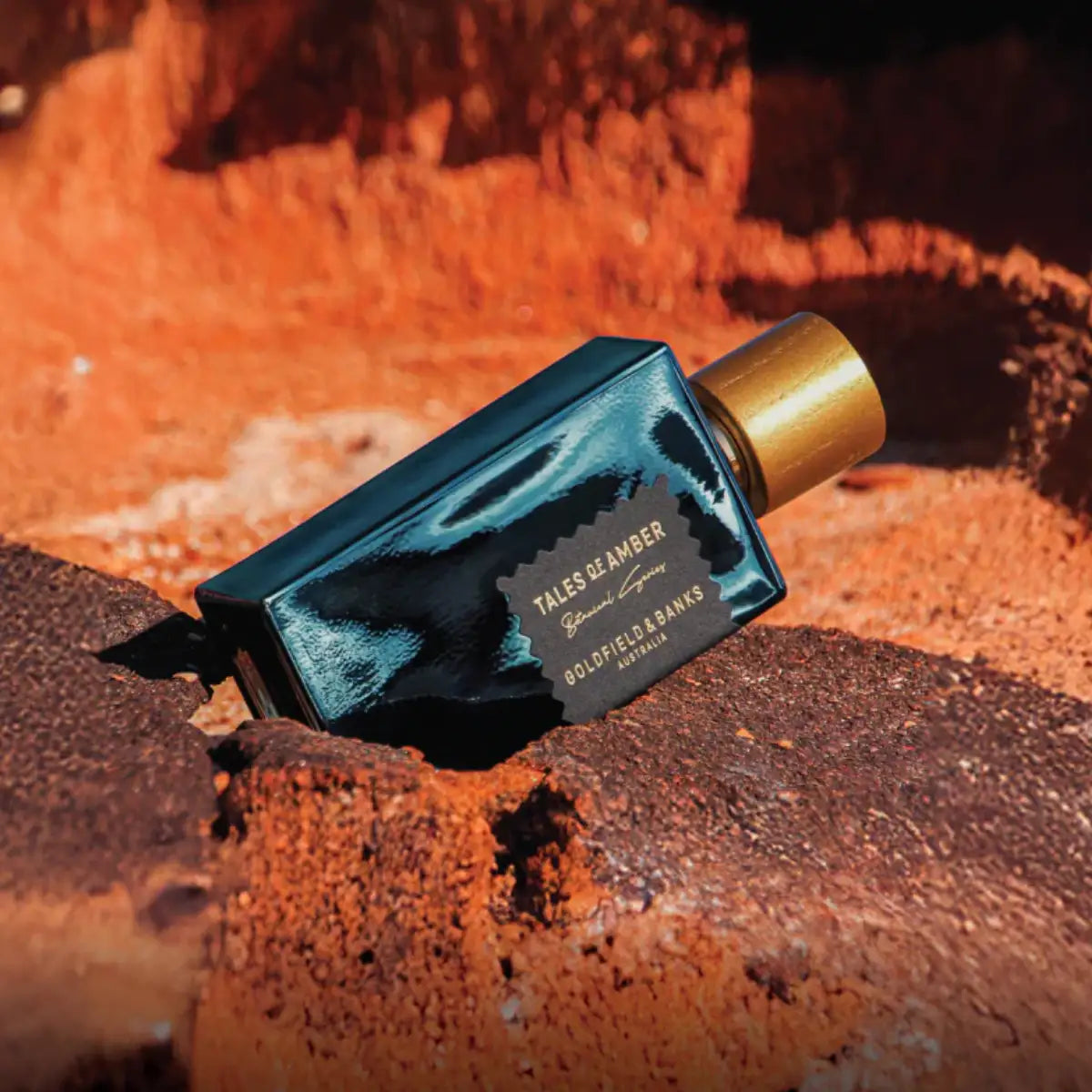 Goldfield & Banks - Tales of Amber Parfumflakon mit dunklem Glas und goldenem Verschluss auf rotem Erdreich