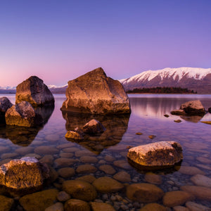 Olfattology - Tekapo ruhiger See mit klaren Wassersteinen und Bergen mit Schnee unter violettem Abendhimmel