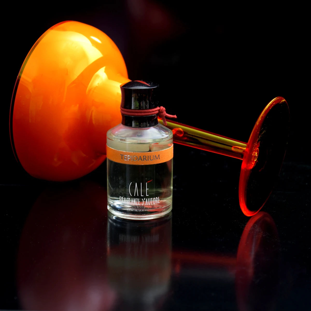 Calé Fragranze d'Autore - Tepidarium Flakon mit orangefarbenem Etikett und schwarzem Verschluss vor dunklem Hintergrund