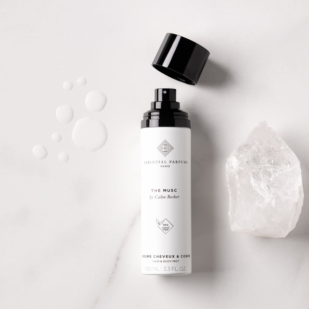 Essential Parfums - The Musc - Hair & Body Mist Sprayflasche mit offenem schwarzen Deckel und Kristall auf hellem Untergrund