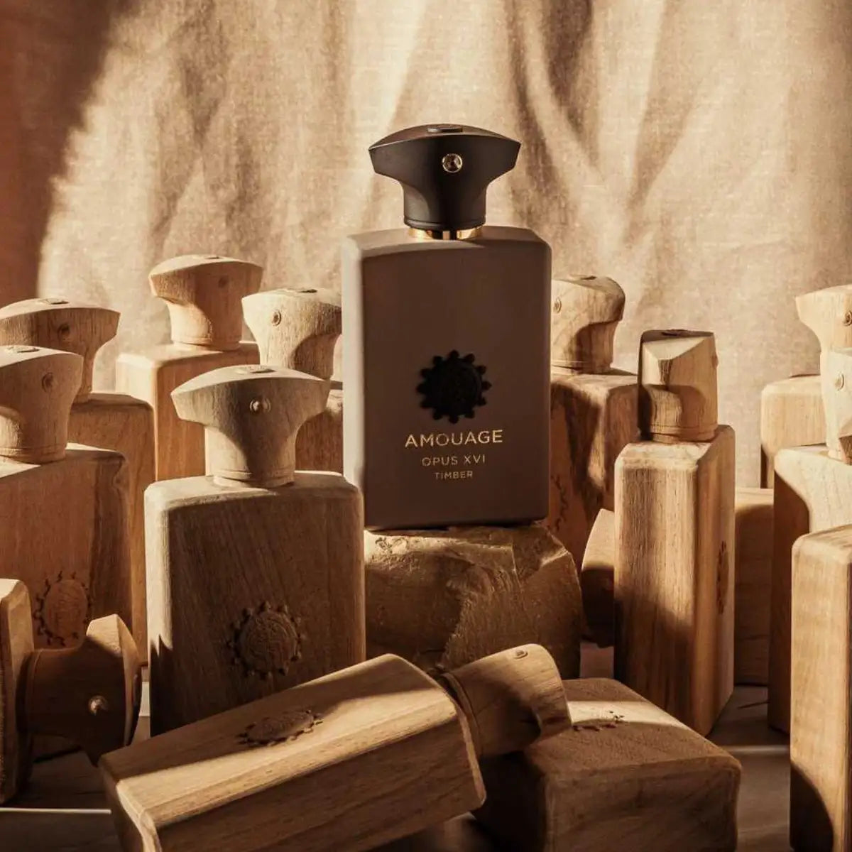 Amouage - Library Collection - Opus XVI - Timber Parfumflakon vor Holzskulpturen und warmem Stoff im Sonnenlicht