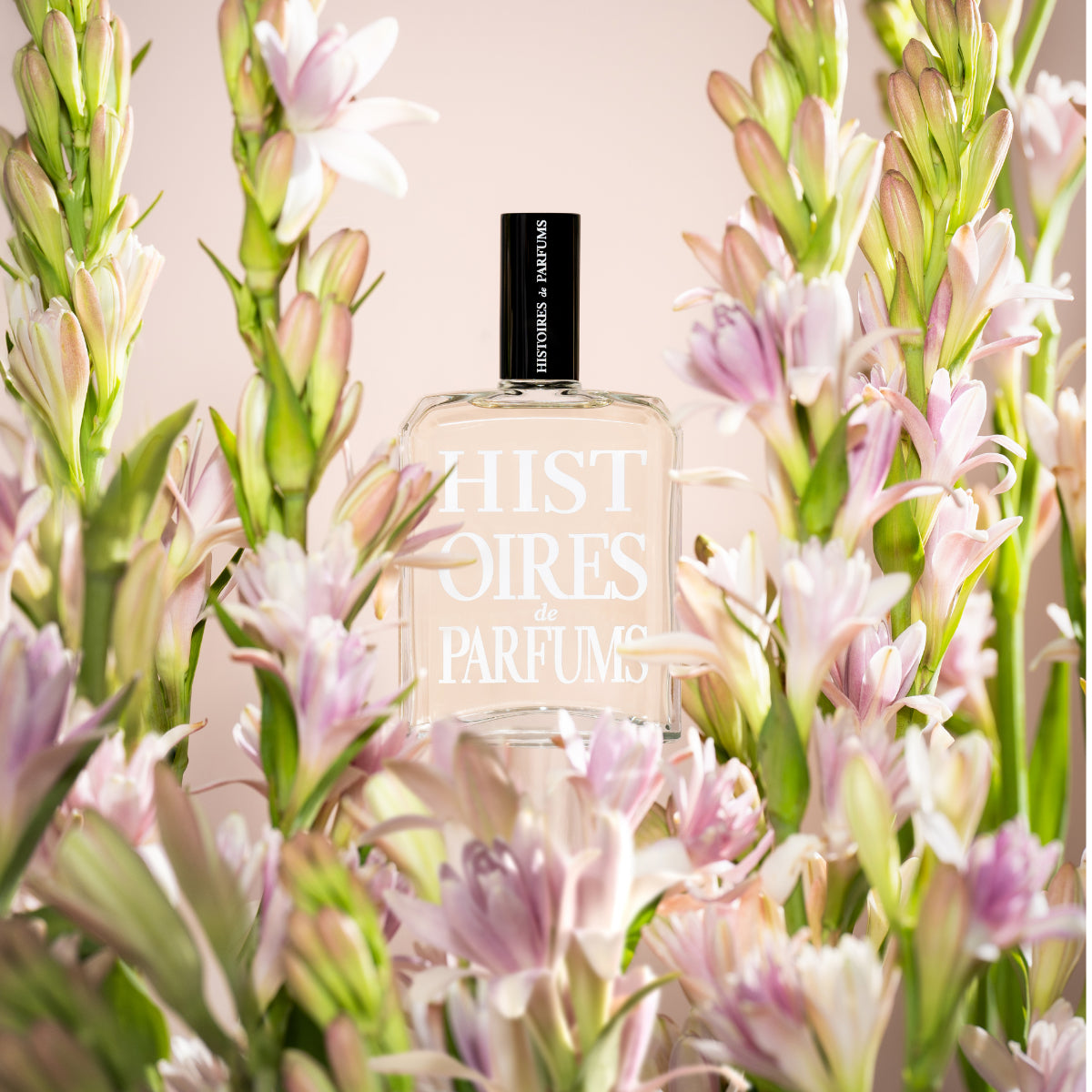 Histoires de Parfums - Tubéreuse Nuit Blanche Parfumflakon umgeben von zarten weißen und rosa Blüten auf hellem Hintergrund