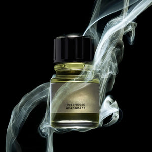 Headspace - Tubereuse Parfumflakon mit gelblichem Inhalt und schwarzem Deckel, umgeben von elegantem Rauch vor dunklem Hintergrund