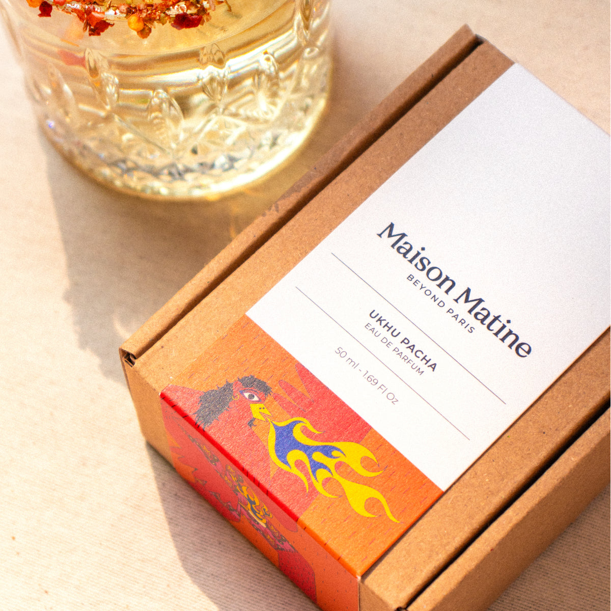 Maison Matine - Ukhu Pacha Verpackung mit farbenfroher Illustration und transparentem Parfumflakon im Sonnenlicht