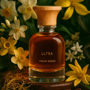Hiram Green - Ultra Parfumflakon mit warmem bernsteinfarbenem Inhalt und naturbelassenem Holzverschluss umgeben von gelben Blumen