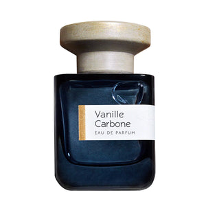 Atelier Materi - Vanille Carbone Parfumflakon in schwarzem Glas mit hellem, rundem Holzverschluss vor weißem Hintergrund