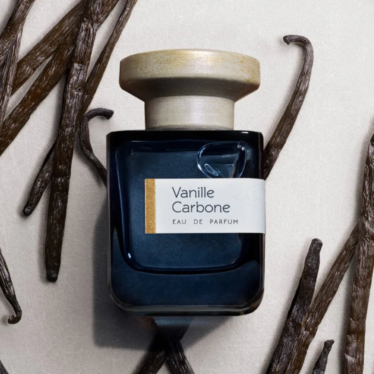 Atelier Materi - Vanille Carbone Parfumflakon in dunklem Glas mit hellem Holzverschluss umgeben von Vanilleschoten