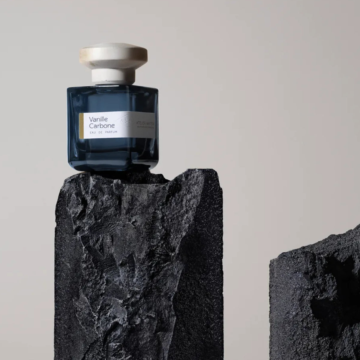 Atelier Materi - Vanille Carbone Parfumflakon in dunklem Glas mit hellem Verschluss auf vulkanischem Gestein