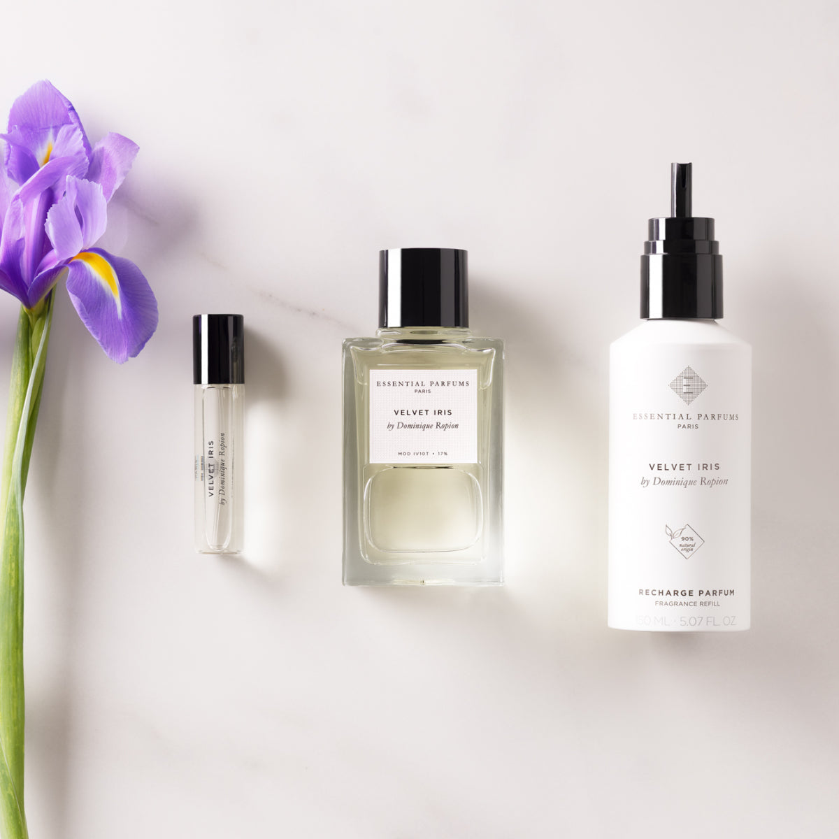 Essential Parfums - Velvet Iris Set mit Parfumflakon, Nachfüllung und Roller auf hellem Untergrund neben lila Irisblüte