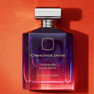 Ormonde Jayne - Verano Parfümflakon in tiefem Blau-Violett mit silberner Kappe vor orangem Hintergrund