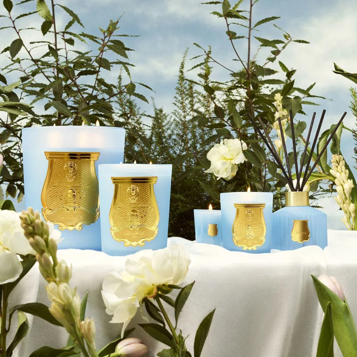 Trudon - Versailles - Diffusor mit blauem Glas und goldfarbenem Emblem vor natürlichem Pflanzenhintergrund