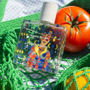 Maison Matine - Warni Warni Parfumflakon mit buntem afrikanischem Design, weißem Verschluss auf grüner Häkeldecke und Tomate
